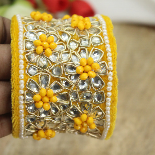 1. Yamini Broad Bracelet by Noori By Nikita in vibrant yellow with exquisite pearl embroidery and intricate kundan work offers a perfect blend of elegance and charm.
2. Crafted with utmost attention to detail, the bracelet not only flaunts a unique design but also ensures ease and comfort during wear.
3.  Its adjustable feature guarantees a perfect fit for any wrist size. The luxurious combination of pearls and kundan elevates the overall look, making it a versatile piece that complements both traditional and contemporary attire.
4. Whether you are attending a grand celebration or a traditional Haldi rasam, this bracelet is specifically crafted to add a touch of grace to your ensemble.
5. Enjoy affordable prices that you can buy online, without compromising on quality, allowing you to find the perfect Bracelet within your budget.